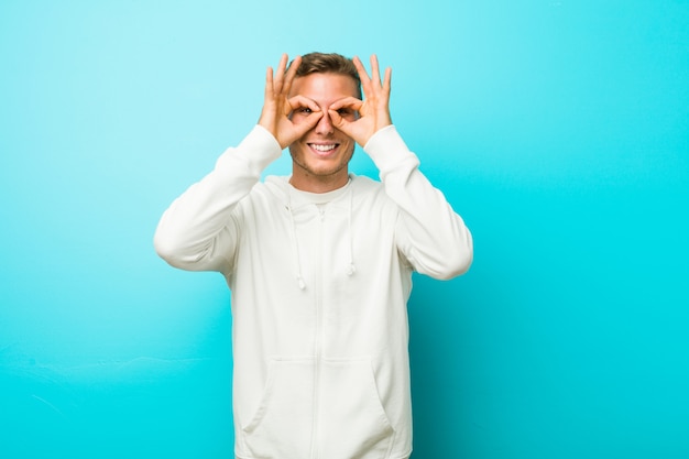 Hombre joven deporte caucásico que muestra bien firmar sobre los ojos