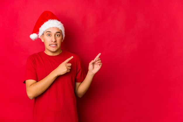 Hombre joven en el día de Navidad sorprendido señalando con los dedos índices a un espacio de copia.