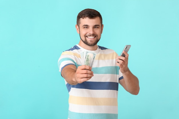 Hombre joven con dinero y teléfono móvil en la superficie de color. Concepto de apuesta deportiva