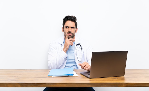 Hombre joven del doctor con su computadora portátil sobre la pared aislada que piensa una idea