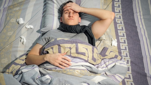 Hombre joven con dolor de cabeza que se despierta en la cama en su casa.