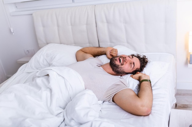 Foto hombre joven durmiendo despertando y estirándose en su cama. concepto de personas, hora de acostarse y descanso - hombre acostado en la cama en casa, es hora de despertar