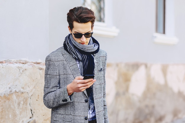 Hombre joven elegante en gafas de sol con el teléfono en la calle