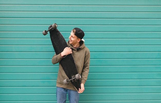 Hombre joven elegante en ropa de calle, sostiene un longboard