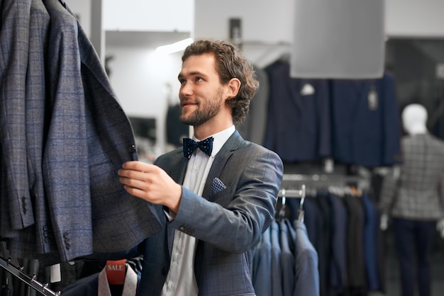 Foto hombre joven eligiendo trajes en boutique.