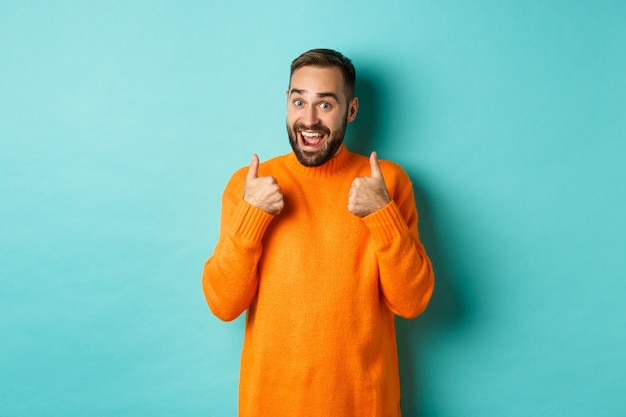 Hombre joven emocionado con barba, mostrando los pulgares hacia arriba en señal de aprobación, elogio o recomendación, de pie