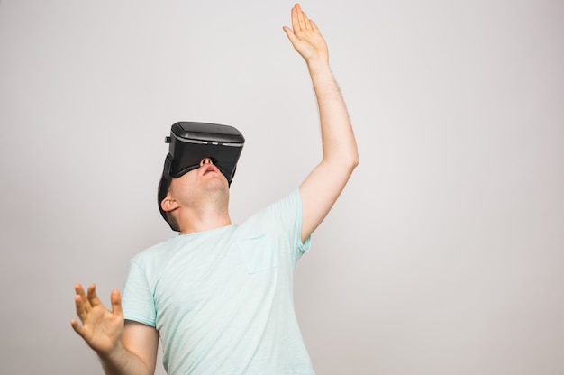 Hombre joven emocionado que usa un auricular VR y experimenta la realidad virtual aislada en gris