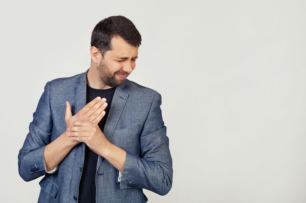 Foto hombre joven empresario con barba en una chaqueta, que sufre de dolor en las manos y los dedos, inflamación de la artritis.