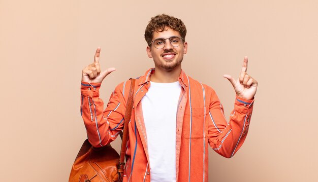 Hombre joven enmarcando o delineando su propia sonrisa con ambas manos, mirando positivo y feliz, concepto de bienestar. concepto de estudiante