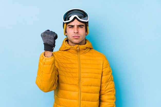 Hombre joven esquiador con gafas de snowboard aislado mostrando puño con agresiva expresión facial.