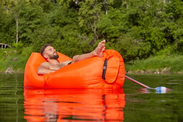 El hombre joven está durmiendo la siesta en un sofá de aire naranja flotando en el río.