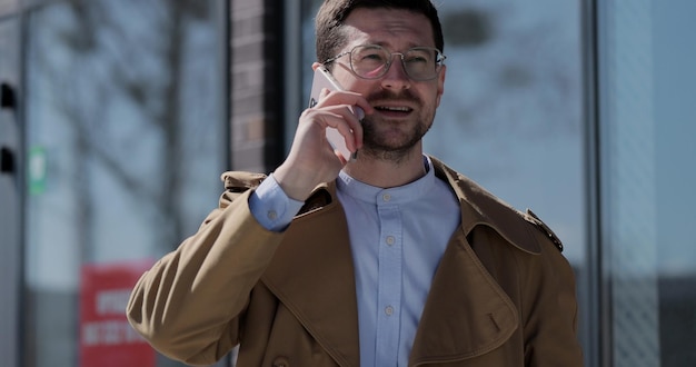 Hombre joven con estilo en gafas hablando por teléfono celular en la calle de la ciudad