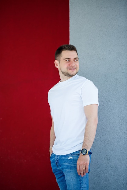 Hombre joven con estilo, un hombre vestido con una camiseta blanca en blanco de pie sobre un fondo de pared gris y rojo. Estilo urbano de ropa, imagen de moda moderna. Moda de hombres