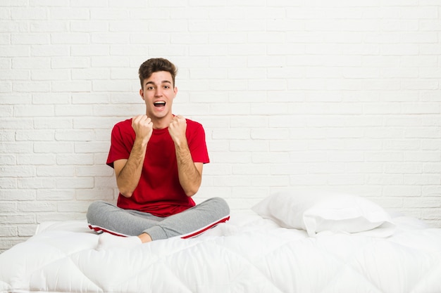 Foto hombre joven estudiante adolescente en la cama animando despreocupado y emocionado. concepto de victoria