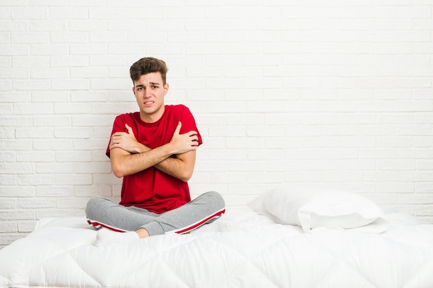 Hombre joven estudiante adolescente en la cama enfriándose debido a la baja temperatura o una enfermedad.