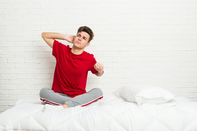 Hombre joven estudiante adolescente en la cama estirando los brazos, posición relajada.