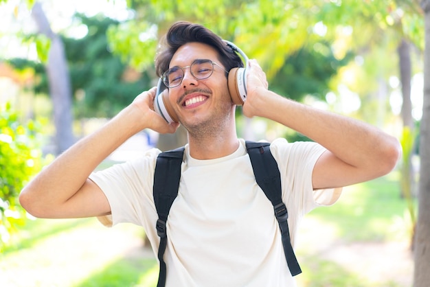 Hombre joven estudiante al aire libre escuchando música