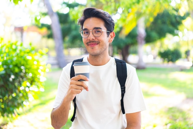 Hombre joven estudiante al aire libre sosteniendo un café para llevar
