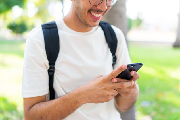 Hombre joven estudiante al aire libre usando teléfono móvil