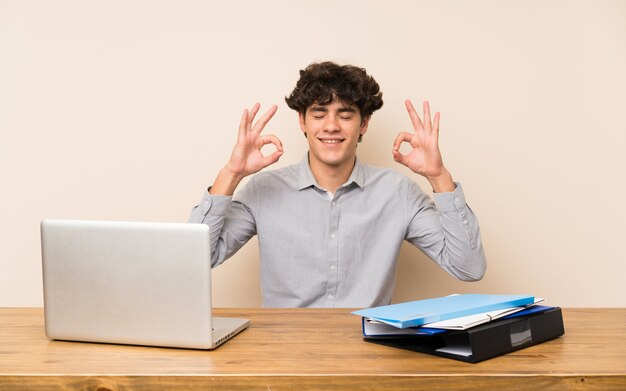 Hombre joven del estudiante con una computadora portátil en actitud del zen