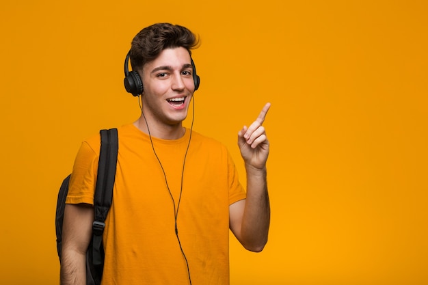 Hombre joven estudiante fresco escuchando música con auriculares apuntando con el dedo como si invitara a acercarse.