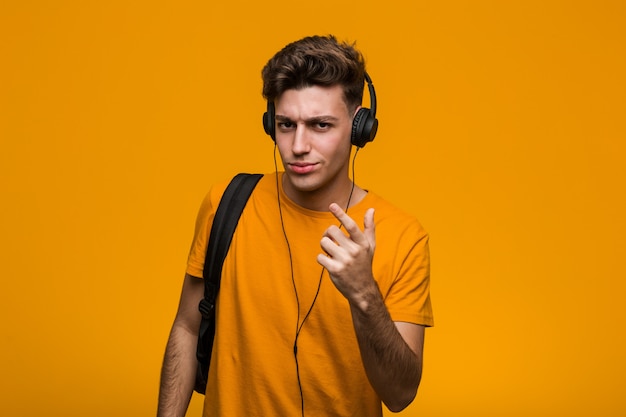 Hombre joven estudiante fresco escuchando música con auriculares impresionado con copia espacio en la palma.