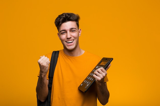 Hombre joven del estudiante que sostiene una calculadora que celebra una victoria o un éxito
