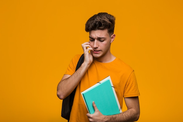 Hombre joven del estudiante que sostiene los libros que cruzan los dedos para tener suerte