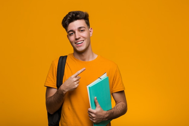 Hombre joven del estudiante que sostiene los libros que señalan con el dedo en usted como si la invitación se acerca.