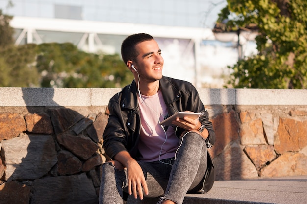 Foto el hombre joven excitó escuchar música en la tableta en las escaleras