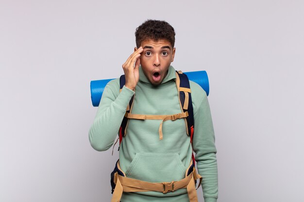 Hombre joven excursionista que parece sorprendido, con la boca abierta, conmocionado, dándose cuenta de un nuevo pensamiento, idea o concepto