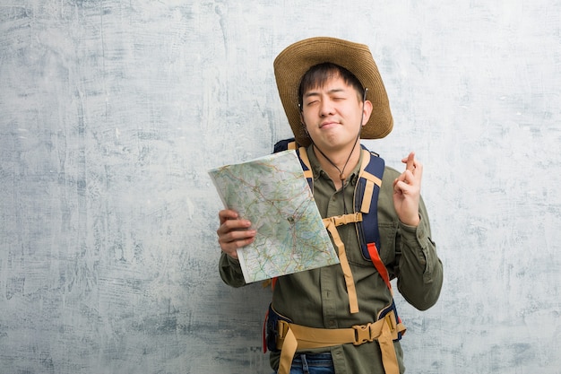 Hombre joven explorador chino sosteniendo un mapa cruzando los dedos para tener suerte