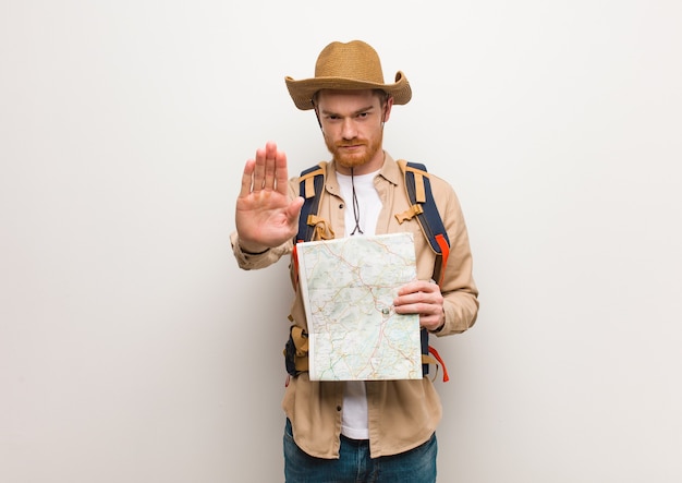 Hombre joven explorador pelirrojo poniendo la mano delante. Sosteniendo un mapa.