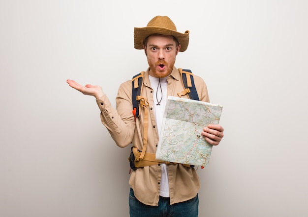 Hombre joven del explorador del pelirrojo que lleva a cabo algo en la mano de la palma. Sosteniendo un mapa