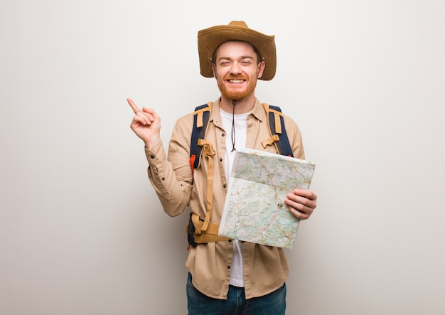 Hombre joven del explorador del redhead que señala al lado con el dedo. Sosteniendo un mapa