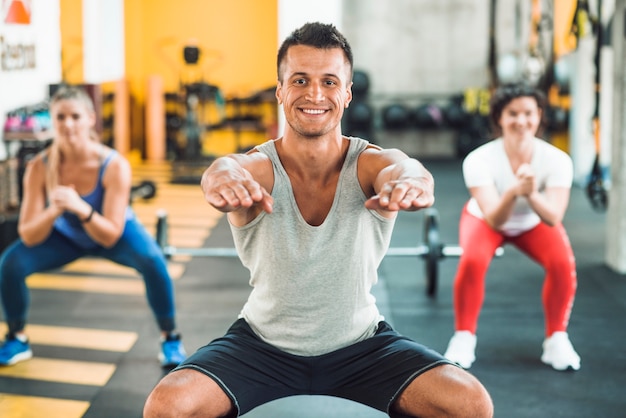 Hombre joven feliz que hace ejercicio del calentamiento en gimnasio