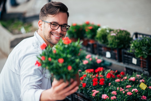 Hombre joven feliz que sostiene las flores hacia cámara y que sonríe al aire libre.