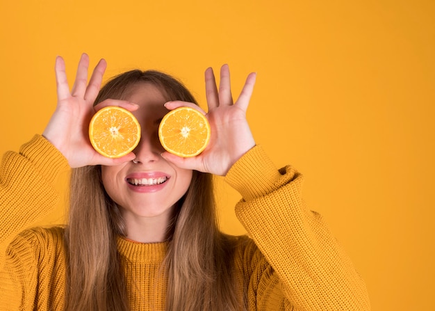 Hombre joven feliz que sostiene las naranjas, los ojos cubiertos en naranja. en la pared de color amarillo pastel