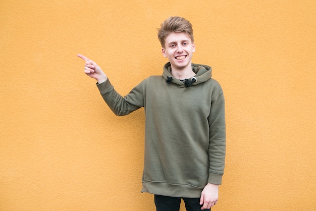 Hombre joven feliz en ropa casual de pie en una pared naranja en una demostración de mano a mano. Copyspace