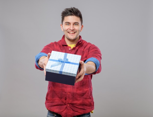 Hombre joven feliz sonriente que presenta un regalo