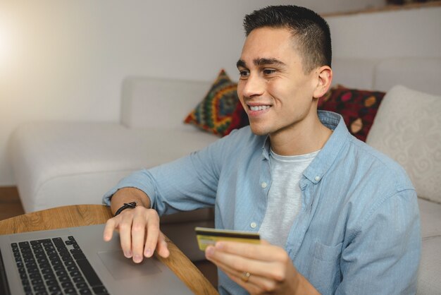 Hombre joven feliz usando la computadora portátil para compras en línea.