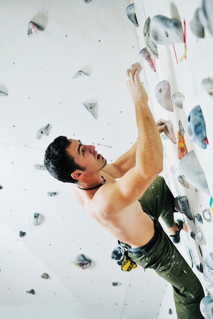 hombre joven y en forma ejercita escalada libre en la pared de práctica interior