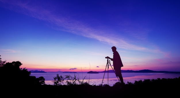 Hombre joven de la fotografía de la silueta tome una foto en salida del sol o puesta del sol paisaje hermoso