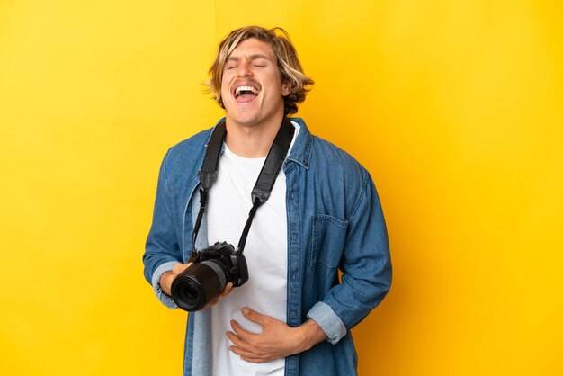 Hombre joven fotógrafo aislado en amarillo sonriendo mucho