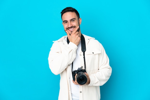 Hombre joven fotógrafo aislado en la pared azul feliz y sonriente