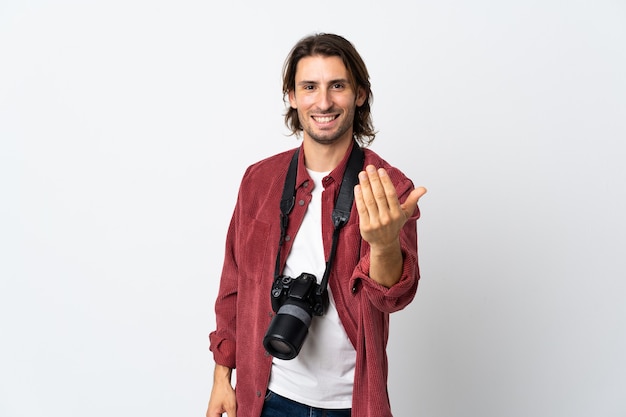 Hombre joven fotógrafo aislado en la pared blanca que invita a venir con la mano.