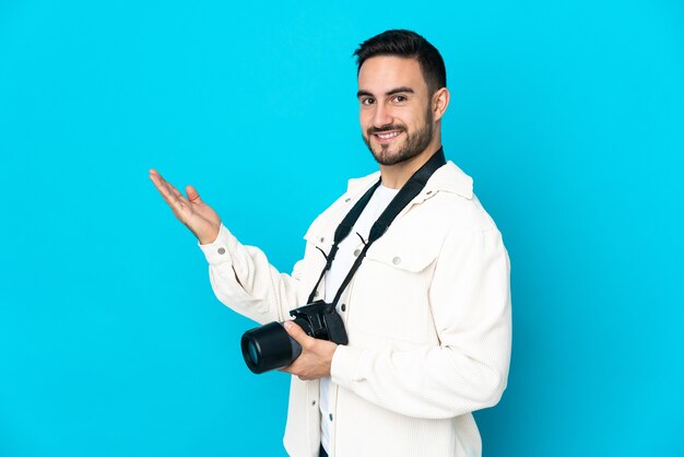 Hombre joven fotógrafo aislado sobre fondo azul extendiendo las manos hacia el lado para invitar a venir