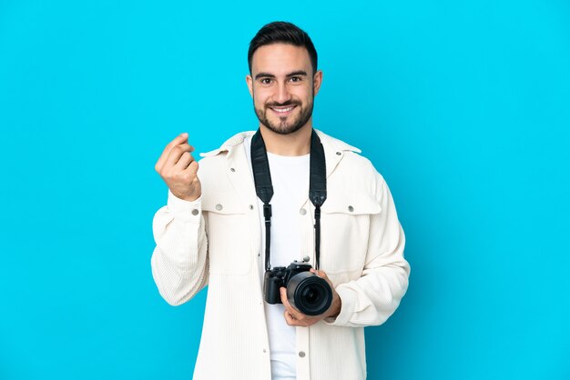 Hombre joven fotógrafo aislado sobre fondo azul haciendo gesto de dinero