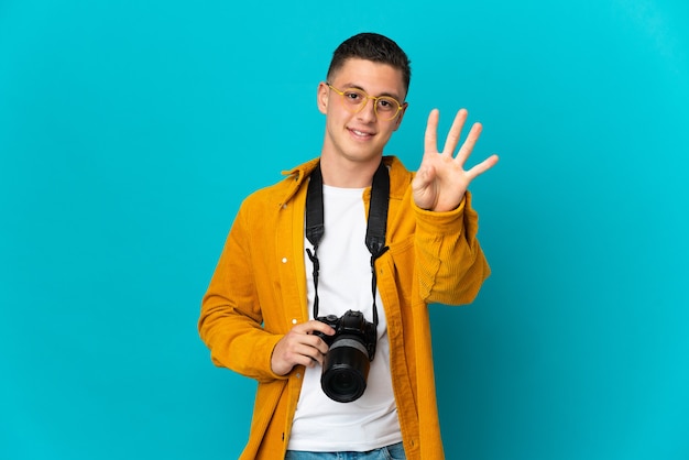 Hombre joven fotógrafo caucásico aislado en la pared azul feliz y contando cuatro con los dedos