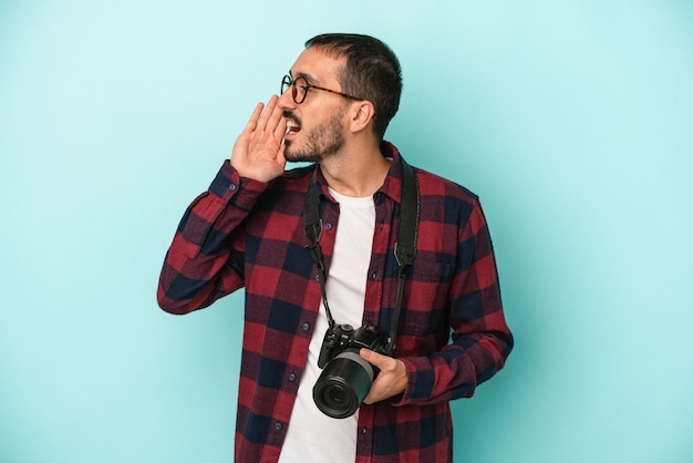 Foto hombre joven fotógrafo caucásico aislado sobre fondo azul gritando y sosteniendo la palma cerca de la boca abierta.